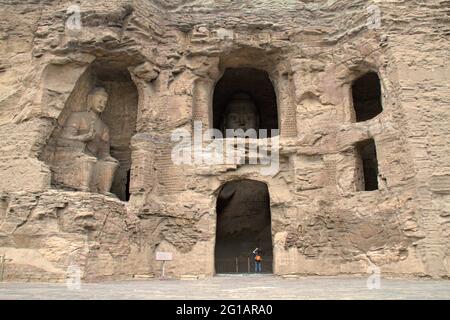 Des images anciennes de Bouddha sculptées dans des grottes de grès et des cavités dans la falaise de la grotte de Yungang près de Datong, Shanxi, Chine, nains un visiteur en contrebas. Banque D'Images