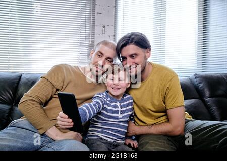 Famille de trois personnes regardant des vidéos sur un smartphone assis sur un canapé Banque D'Images