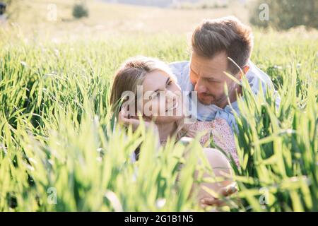 Flirter et sourire de jeune belle blonde à la première date avec l'homme. Photo de couple assis dans une herbe verte luxuriante Banque D'Images