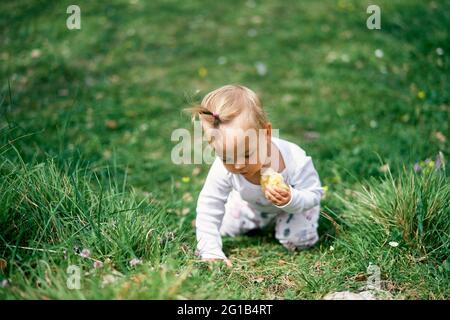 La petite fille est assise sur ses genoux, penchée vers l'avant sur un pré vert avec une pomme dans sa main Banque D'Images