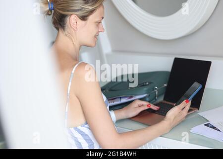 Elle travaille sur un ordinateur portable et lit les actualités sur son smartphone Banque D'Images