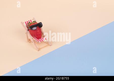 Idée créative drôle faite de chaise de pont et de fraise avec des lunettes de soleil sur une plage. Concept de vacances d'été minimum. Banque D'Images