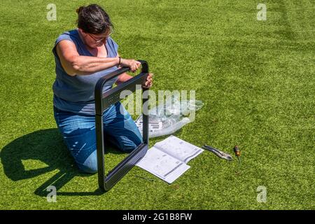 Femme construisant un barbecue d'auto-assemblage à l'extérieur avec des outils et un ensemble d'instructions. Banque D'Images