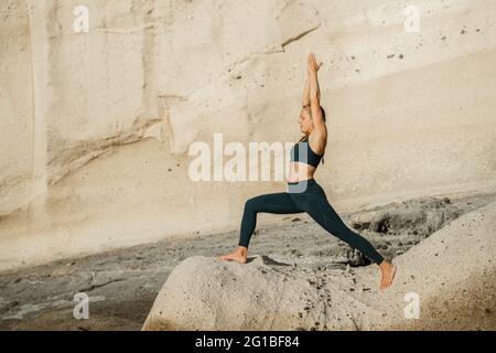 Les jeunes femmes pieds nus dans les vêtements de sport pratiquant le yoga sur Crescent posent contre la montagne rocheuse en plein soleil Banque D'Images