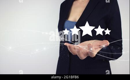 Concept d'évaluation du service produit. Tenir à la main l'hologramme numérique cinq étoiles sur fond gris. Client qui donne une note cinq étoiles. Banque D'Images