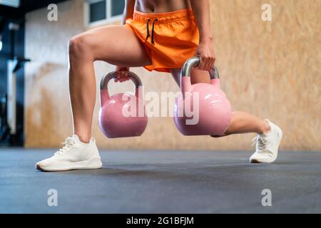 Une athlète féminine court et non reconnaissable effectuant une fente avant pendant l'entraînement avec des poids contre la barbell dans la salle de sport Banque D'Images