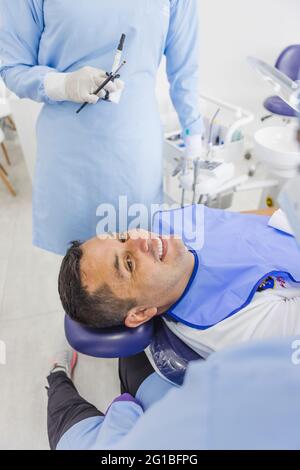 Homme souriant parlant aux femmes médecins en uniforme après une intervention dentaire en clinique Banque D'Images