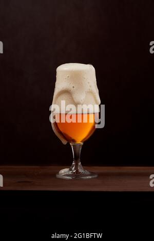 Bière mousse fraîchement brassée en verre tulipe placée sur un comptoir en bois sur fond marron Banque D'Images