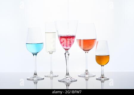 Cocktails colorés assortis dans des verres en cristal de forme différente servis sur table miroir sur fond blanc Banque D'Images