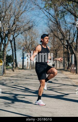 Un athlète masculin de sport sautant avec une corde à sauter et regardant loin sur la passerelle pendant l'entraînement cardio dans le parc Banque D'Images