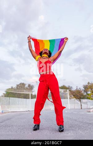 De dessous de l'élégant Afro-américain femelle dans le port tendance élevant drapeau avec l'ornement arc-en-ciel tout en regardant vers le haut sur la chaussée Banque D'Images