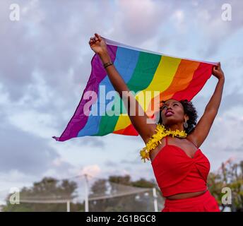 De dessous de l'élégant Afro-américain femelle dans le port tendance élevant drapeau avec l'ornement arc-en-ciel tout en regardant vers le haut sur la chaussée Banque D'Images