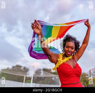 De dessous de l'élégant Afro-américain femelle dans le port tendance élevant drapeau avec l'ornement arc-en-ciel tout en regardant la caméra sur la chaussée Banque D'Images