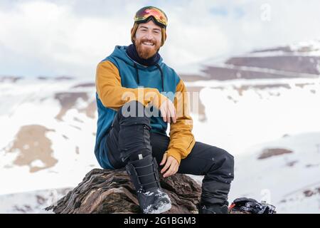 Athlète masculin souriant en vêtements de sport regardant l'appareil photo tout en étant assis sur le support en hiver en Espagne Banque D'Images