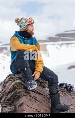 Athlète masculin barbu dans des vêtements de sport regardant loin en étant assis sur le mont en hiver en Espagne Banque D'Images