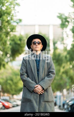 Jeune homme transgenre en manteau classe et chapeau regardant loin dans la lumière du jour Banque D'Images