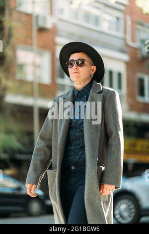 Jeune homme transgenre en manteau classe et chapeau regardant loin dans la lumière du jour Banque D'Images