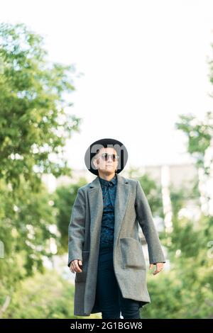 Jeune homme transgenre en manteau classe et chapeau regardant loin dans la lumière du jour Banque D'Images