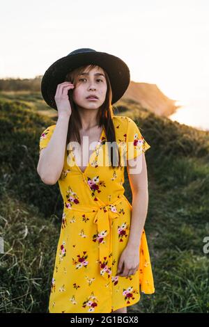 Belle jeune femme en sundress jaune et chapeau debout sur verdant prairie dans la campagne ensoleillée Banque D'Images