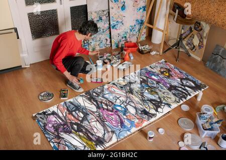 De dessus de l'artiste anonyme masculine mélangeant des peintures sur le sol contre des peintures abstraites dans l'atelier Banque D'Images