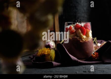 Bol à smoothie appétissant avec fraises granola et bleuets placés sur une table près de diverses fleurs sauvages Banque D'Images