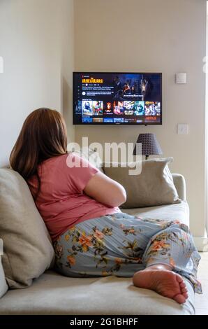 Une dame se détend sur un canapé et sélectionne un film à regarder sur Netflix. Diffusé à la télévision sur Internet. Banque D'Images