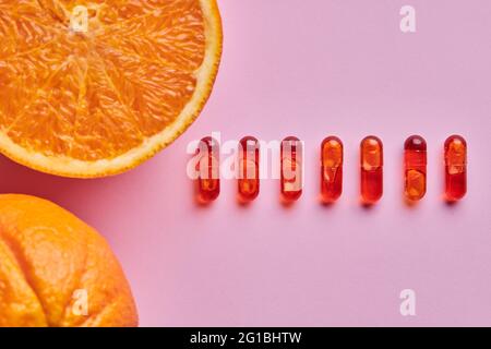 Vue de dessus composition d'oranges mûres coupées disposées sur une surface rose près d'une rangée de pilules Banque D'Images