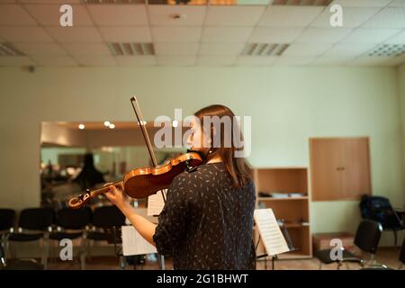 Vue arrière d'une musicienne professionnelle concentrée jouant du violon acoustique et regardant une feuille de musique pendant la répétition en studio Banque D'Images