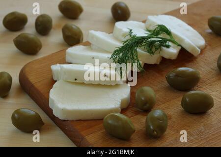 Le fromage traditionnel de Chypre appelé halloumi décoré d'herbes vertes et d'olives, sur un plateau de cuisine en bois et une table de près Banque D'Images