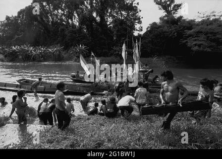 Kalimantan occidental, Indonésie. Mars 2007. Un homme décharge un jeu d'instrument de percussion gamelan, alors qu'il passe devant une foule de gens - la communauté Dayak Tamambaloh - qui s'éclaboussent de l'eau les uns sur les autres comme un acte purifiant, devant un bateau qui vient de transporter la famille de leur nouveau chef traditionnel pour une visite au lieu de sépulture de leur ancien chef dans le village de Sungai Uluk Palin (Sungulo Palin), Putusibau Utara, Kapuas Hulu, West Kalimantan, Indonésie. Banque D'Images