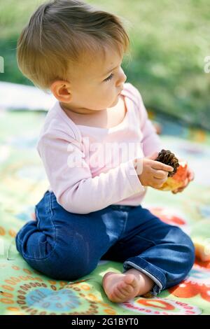 La petite fille est assise sur une couverture colorée et tient un cône de pin et une pomme dans ses mains. Gros plan Banque D'Images