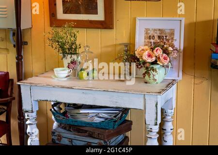 Une collection d'articles décoratifs vintage placés sur une ancienne table en bois avec des valises et des magazines en dessous Banque D'Images