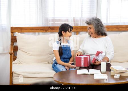 Grand-mère asiatique et petite-fille ouvrent la boîte cadeau rouge dans le salon à la maison pendant le festival du nouvel an ou la fête d'anniversaire. Moment de bonheur et fami Banque D'Images