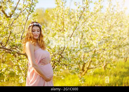 Belle femme enceinte tient les mains sur le ventre dans le jardin de printemps. Banque D'Images