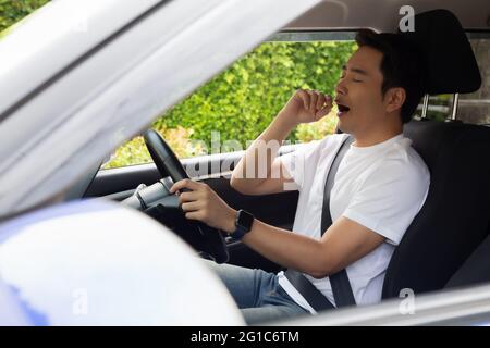 Un jeune homme fatigué dorment en voiture, le travail dur cause une mauvaise santé, s'assoir pendant que la voiture est sur un feu rouge, un bourrage de circulation ou un concept surtravaillé Banque D'Images