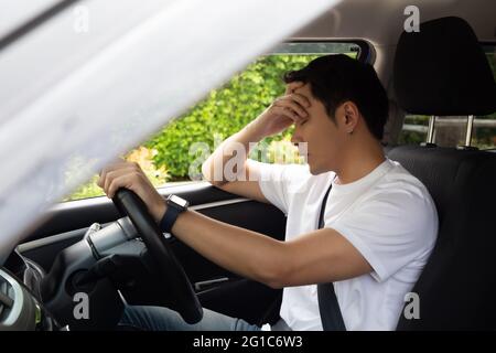 Un jeune homme fatigué dorment en voiture, le travail dur cause une mauvaise santé, s'assoir pendant que la voiture est sur un feu rouge, un bourrage de circulation ou un concept surtravaillé Banque D'Images