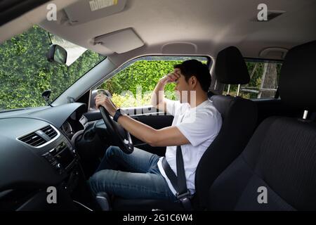 Un jeune homme fatigué dorment en voiture, le travail dur cause une mauvaise santé, s'assoir pendant que la voiture est sur un feu rouge, un bourrage de circulation ou un concept surtravaillé Banque D'Images