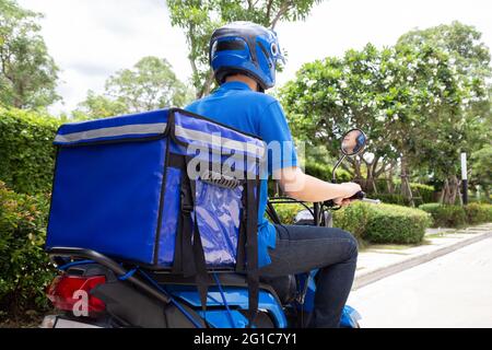 Le liveur porte une moto bleue uniforme et une boîte de livraison. Moto proposant un service de restauration express Banque D'Images