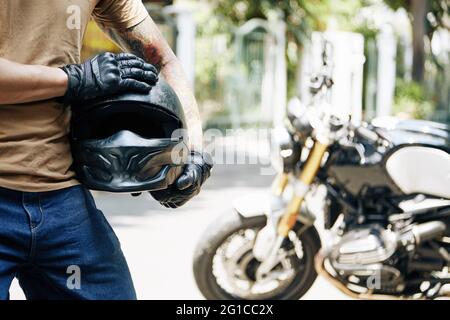 Image rognée d'un motocycliste en gants de cuir tenant son casque, sa moto est en arrière-plan Banque D'Images