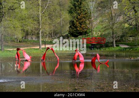 Le Pont rouge en bois et la sculpture en vagues sur le lac Nessie au parc de sculptures et jardins de l'Himalaya, Grewelthorpe, Ripon, North Yorkshire, Angleterre. Banque D'Images