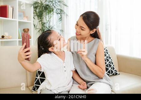 Petite fille regardant sa mère faire le geste de paix quand ils photographient ou filment de la vidéo pour les médias sociaux Banque D'Images