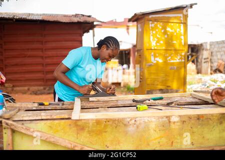 belle femme africaine sourit alors qu'elle utilise un avion de cric pour habiller le bois en taille Banque D'Images