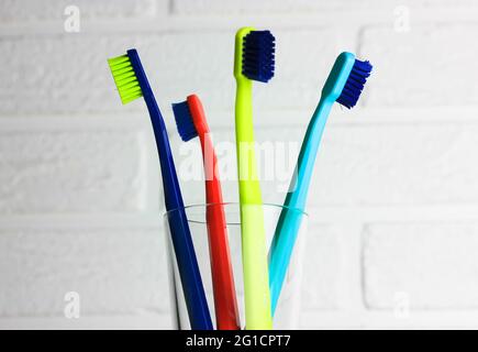 Jeu de brosses à dents multicolores en plastique - vert, bleu, rouge, violet - en verre transparent sur fond blanc. Tasse avec quatre couleurs vives SO Banque D'Images