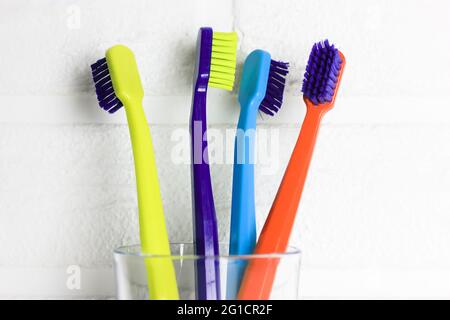 Jeu de brosses à dents multicolores en plastique - vert, bleu, rouge, violet - en verre transparent sur fond blanc. Tasse avec quatre couleurs vives SO Banque D'Images