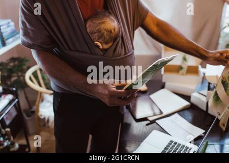 Section médiane de l'ensemble de maintien professionnel masculin avec fils dans un porte-bébé au bureau à domicile Banque D'Images