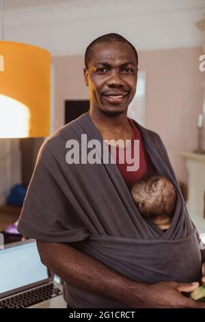 Portrait d'un homme d'affaires souriant transportant un enfant dans un porte-bébé à la maison Banque D'Images