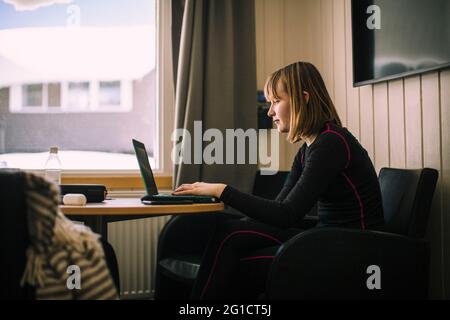 Adolescente utilisant un ordinateur portable tout en faisant des devoirs dans le salon Banque D'Images