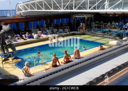 Passagers autour de la piscine couverte sur un paquebot de croisière avec le toit couvrant rétracté pour permettre le soleil dans, Caraïbes Banque D'Images