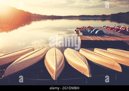 Kayaks et bateaux à aubes au bord d'un lac au coucher du soleil, virage de couleur appliqué. Banque D'Images