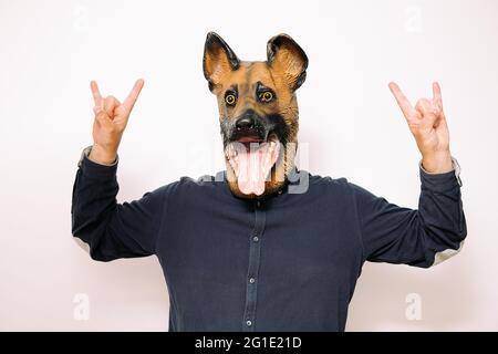 personne portant un masque pour chien et faisant le signe des cornes avec les deux mains sur fond blanc, concept d'une mascotte heureuse et énergique Banque D'Images